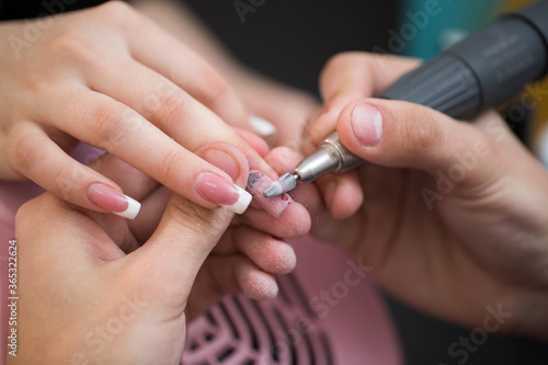 Closeup shot of master uses an electric machine to remove the nail polish during manicure in the salon. Hardware manicure. Concept of body care