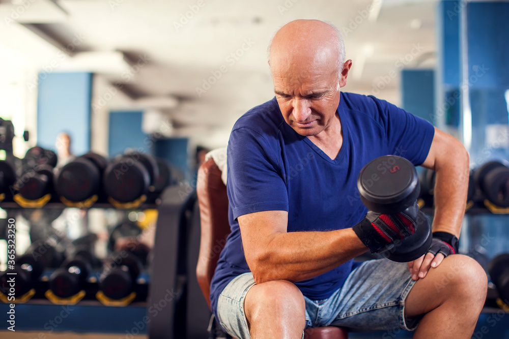 A portrait of senior man in the gym training with dumbbells. People, health and lifestyle concept A portrait of senior man in the gym training with dumbbells. People, health and lifestyle concept