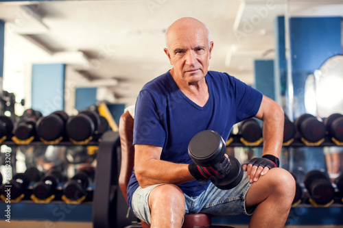 A portrait of senior man in the gym training with dumbbells. People  health and lifestyle concept