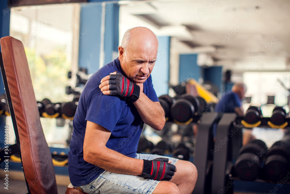 A portrait of senior man feeling strong shoulder pain during training in the gym. People, healthcare and lifestyle concept A portrait of senior man feeling strong shoulder pain during training in the gym. People, healthcare and lifestyle concept