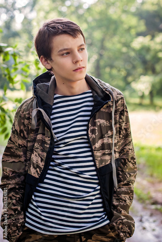 Fotografie Teenager boy in a vest and camouflage jacket, portrait outdoors, looking to the
