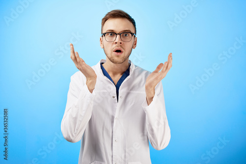 Shocked doctor in white coat opened his mouth in surprise isolated on blue background