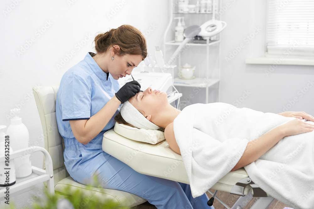 Obraz premium Doctor cosmetologist makes a multi-stage facial cleansing procedure to a young attractive woman in a beauty salon. Summer skin care