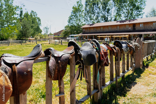 Many leather saddles on wooden fence and ready to put on the horseback photo