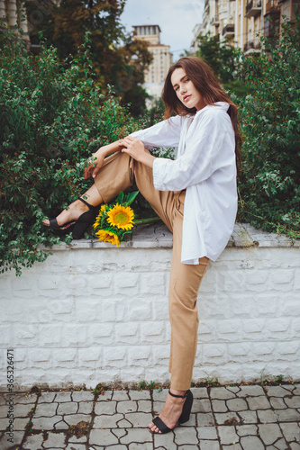 Obraz na płótnie Young happy beautiful girl is walking in a shirt and pants with a bouquet of flowers of sunflowers on a city street w salonie