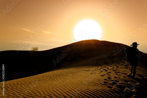 sunset over the sand dunes in the Gobi Desert in Inner Mongolia  China. sandy desert with blue sky and apparent sun  few clouds  extraordinary travel scene. majority color orange   yellow  orange sky