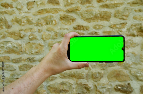 man hand holding a phone horizontally in front of an old stone wall.