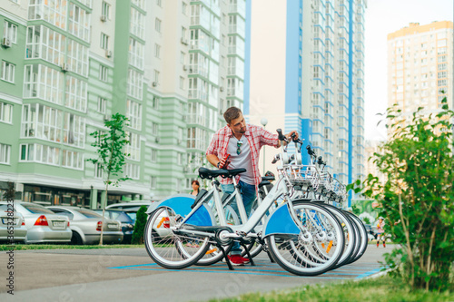 Male tourist chooses a bicycle in the parking lot of Schering. A man rents a bicycle from a row on a background of colored buildings. Bicycle rental for walking