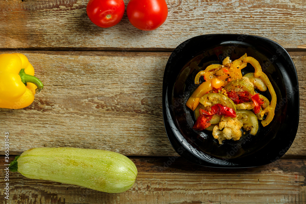 Vegetable stew stew on a black plate and a number of vegetables on a wooden table. Vegetable stew stew on a black plate and a number of vegetables on a wooden table.