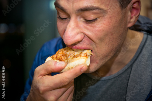 The man eating pizza. It s in the cafe. Holding a piece of pizza in hand  close-up.