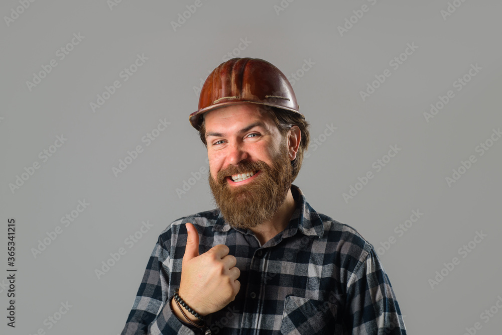 Smiling worker in hard hat shows thumb up. Construction worker. Builder concept. Building, industry, technology. Builder in hard hat. Portrait of bearded workman. Advertising.