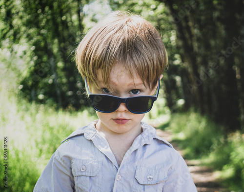 Happy little boy with sunglasses outdoors in park.