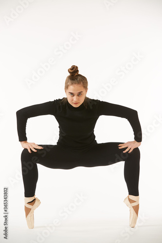 A girl in black clothes and Pointe shoes on a white isolated background performs dance and ballet poses and movements.