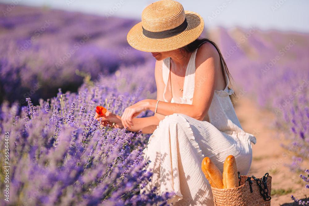 Woman in lavender flowers field at sunset in white dress and hat