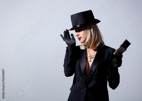 Blonde woman in vintage black jacket and top hat with chocolate bar on white background