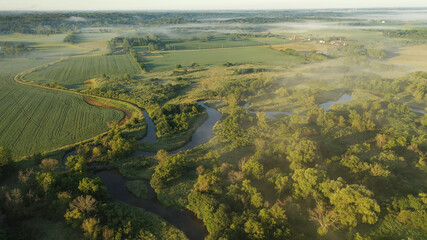 Acrylglasbilder Pistache Aerial view of rural landscape with lush greenery, trees, river in the foreground and farmhouse, farmland in the background. American midwestern countryside scenery in the early sunny morning, summer  © alenamozhjer