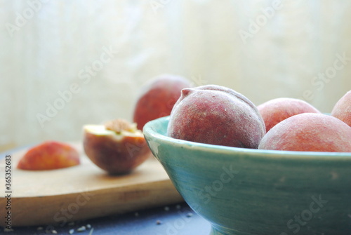 Fresh organic peaches served in a handmade turquoise ceramic bowl and few sliced pieces of peaches on the wooden cutting board.