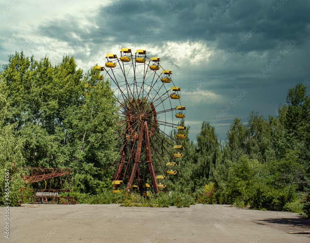 Iconic pripyat ferris wheel seen from the open area in front of it. No people around. Dramatic cloudy day during the summer in the exclusion zone