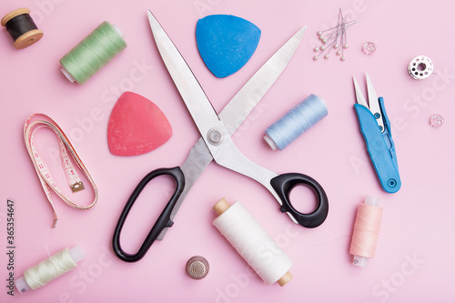 Top view of scissors, threads and sewing supplies on a pink background. The concept of sewing clothes.
