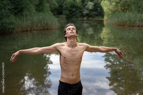 Shirtless man with arms outstretched standing against lake in forest
