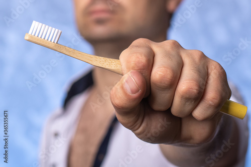 bamboo toothbrush in a man's hand close-up. a man in focus in the background. biodegradable hygiene items. eco friendly concept.