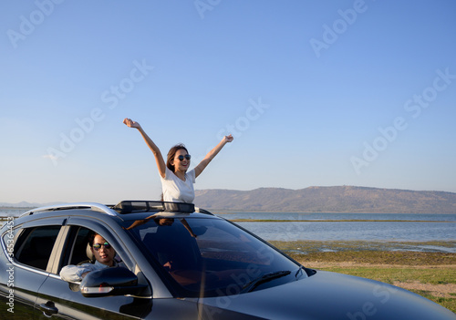 Asian woman in car with raised hands driving on sunset