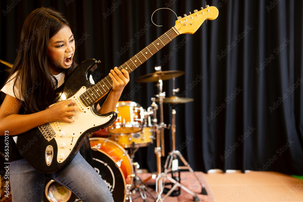 Fototapeta premium A cute young Asian elementary school girl with long hair playing with serious electric guitar in rock songs.