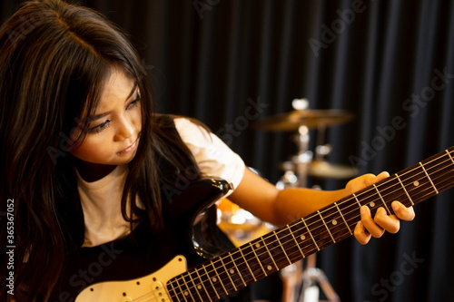 A cute Asian elementary school girl who has long hair and is seriously playing an electric guitar for a rock song.