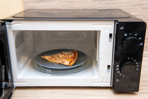 Plate with slice of pizza in microwave oven