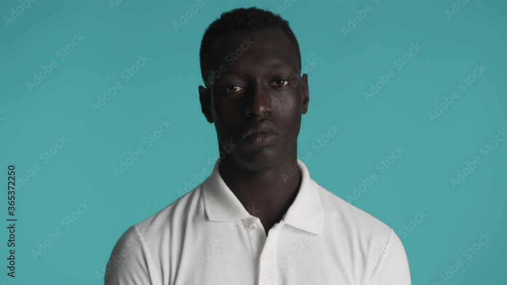 Young serious African American man in T-shirt confidently looking in camera over colorful background. Face expression Young serious African American man in T-shirt confidently looking in camera over colorful background. Face expression