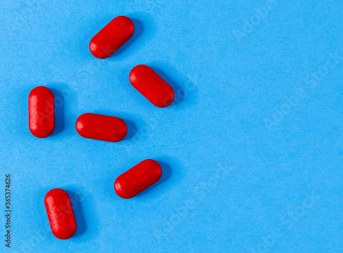 Six red pills are scattered to the left against a blue background and with space for text on the right, top view close-up.