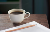 A white coffee cup with hot steam floating on a gray table in the morning for work at home, with pencils and white paper as a component, with copy space for text.