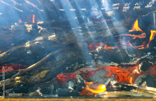 Ray of sunshine through burning firewood metal grill. Soft focus.