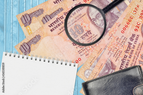 10 Indian rupees bills and magnifying glass with black purse and notepad. Concept of counterfeit money. Search for differences in details on money bills to detect fake photo