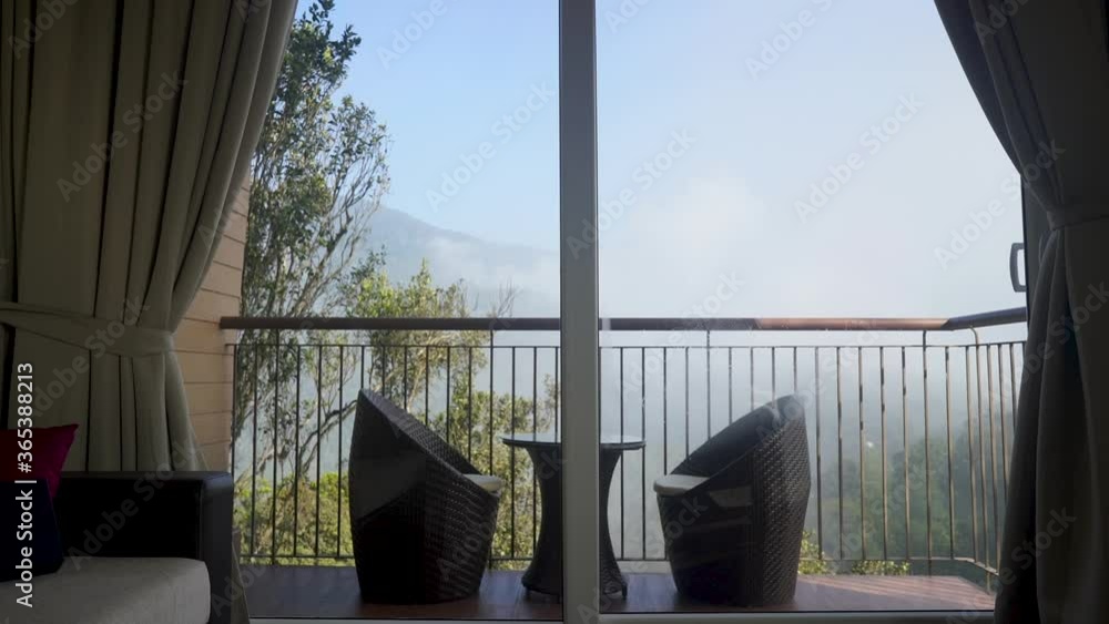 Cozy Chairs And Table Behind The Glass Door At The Balcony Of Shola Crown Luxury Hotel With A Cloudy Mountain View In Bodimettu, Kerala, India. - static shot Cozy Chairs And Table Behind The Glass Door At The Balcony Of Shola Crown Luxury Hotel With A Cloudy Mountain View In Bodimettu, Kerala, India. - static shot