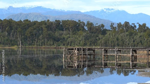 Lake Mahinapua in the South Island of New Zealand on a still day with the jetty, trees and mountains reflecting