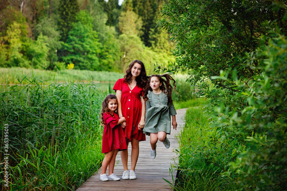 Obraz premium Family portrait of a large friendly family. A Caucasian pregnant mother and two children stand together in a Park on a wooden bridge. A young pregnant mother with a family in the countryside.