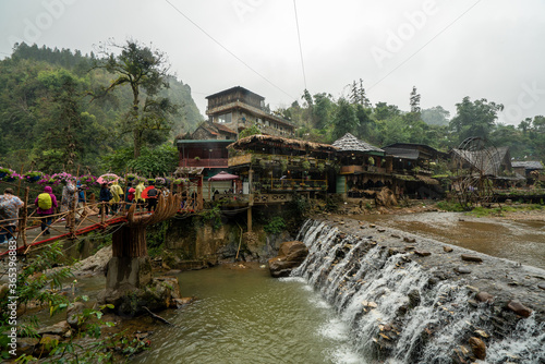 Tourists with umbrellas cross bridge at Cat Cat Resort in Sapa, Vietnam