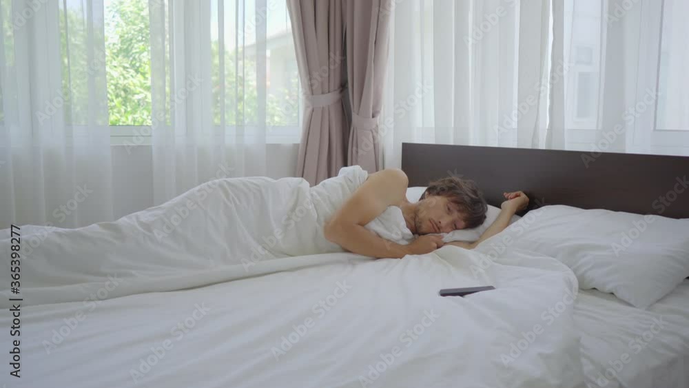 A young man happily wakes up in bed and checks out his phone A young man happily wakes up in bed and checks out his phone