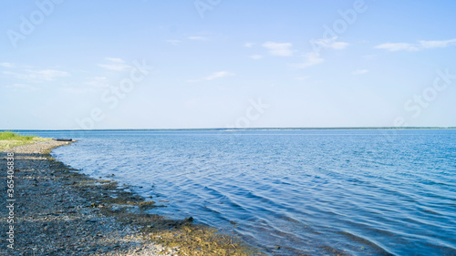 Stone shore with slime on a hot summer evening. An inflatable boat can be seen in the distance. Blooming salt lake in Russia. Small waves on the water.