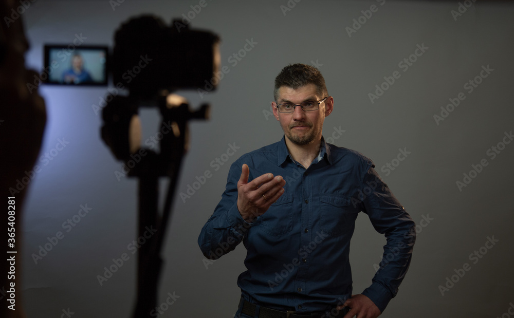 professional actor plays role of confused man and raises hand in front of blurry black camera on tripod close view professional actor plays role of confused man and raises hand in front of blurry black camera on tripod close view