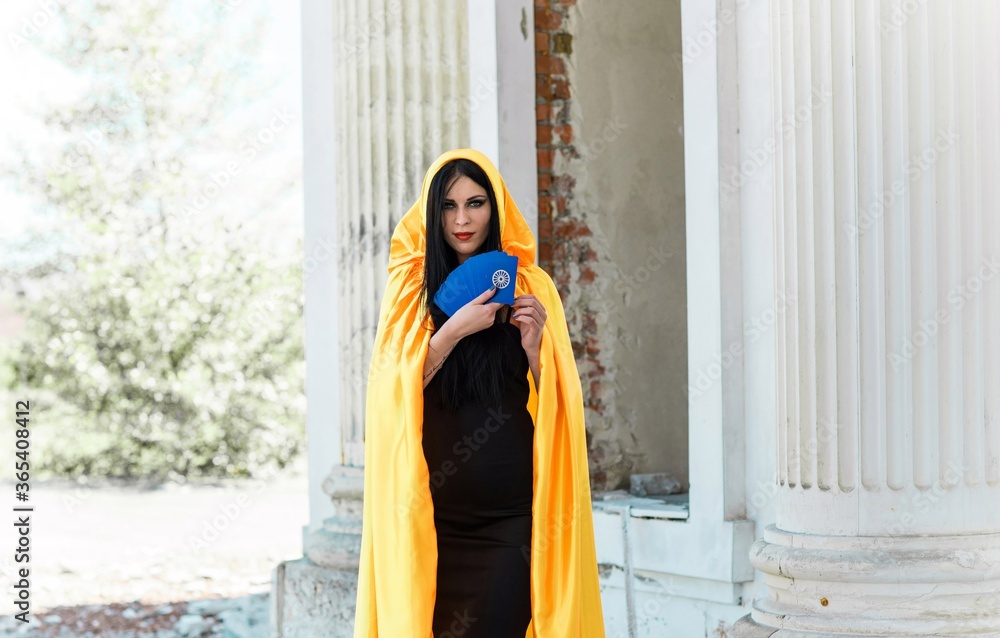 Mystical woman in yellow cloak, black dress, and tarot cards at old town, Halloween date, party outfit 