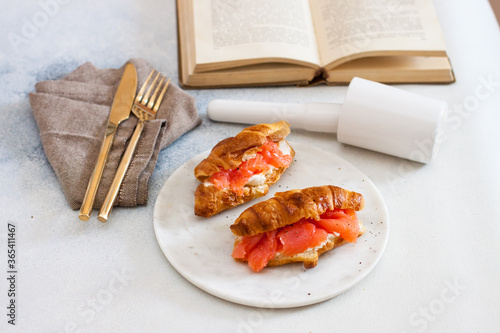 Delicious breakfast with croissant, smoked salmon, cheese and pepper on white plate. Opened old book on the background.