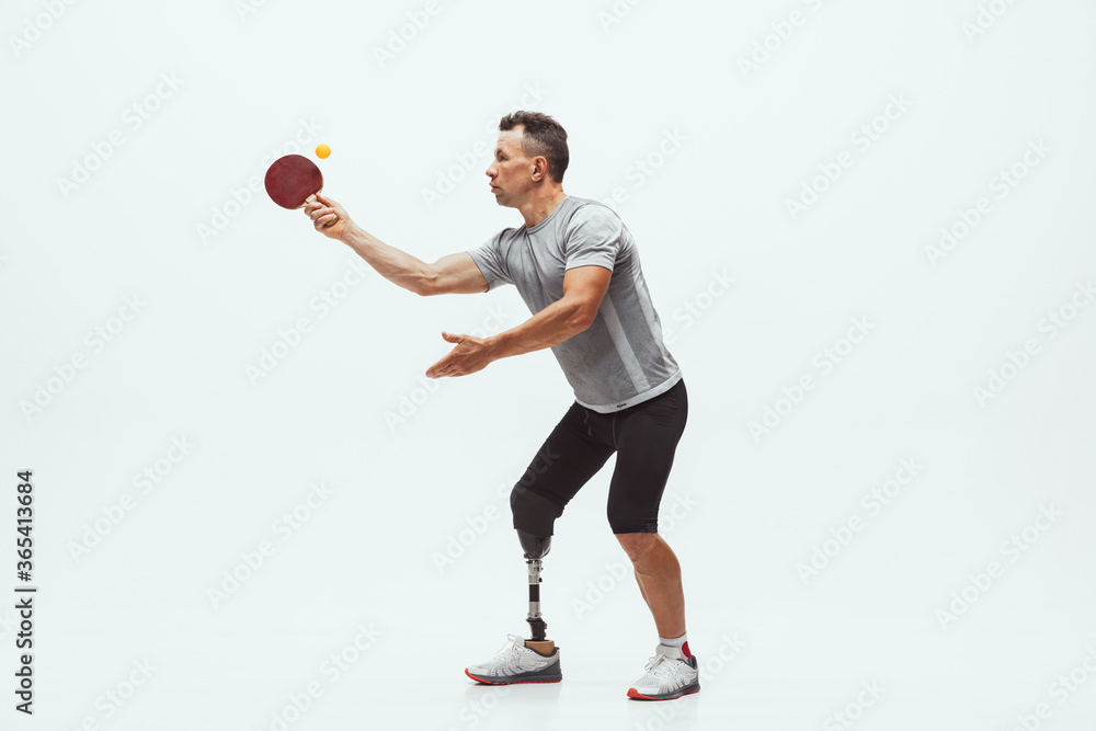 Athlete with disabilities or amputee isolated on white studio background. Professional male table tennis player with leg prosthesis training in studio. Disabled sport and healthy lifestyle concept. Athlete with disabilities or amputee isolated on white studio background. Professional male table tennis player with leg prosthesis training in studio. Disabled sport and healthy lifestyle concept.