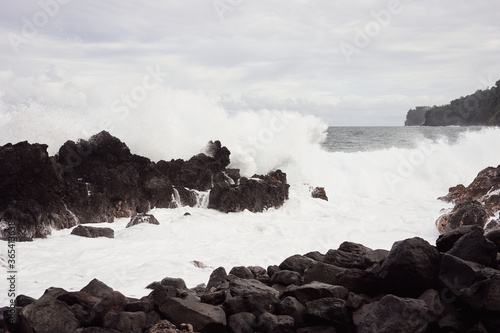 Wave splashing against lava rocks on a lava beach on the Big Island of Hawaii.