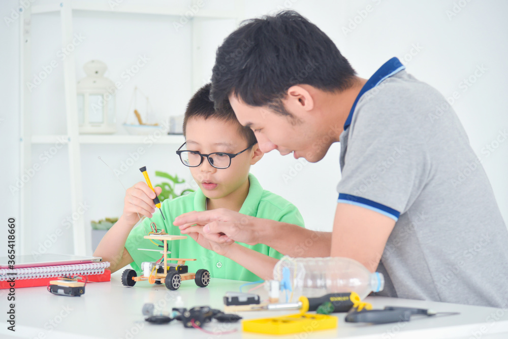 Happy boy helping his father while creating electric wooden toy car and enjoying time together in livining room at home. Happy boy helping his father while creating electric wooden toy car and enjoying time together in livining room at home.
