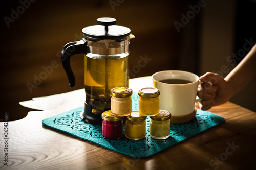 Morning tea with honey. Hands of a boy, a teapot with tea, jars of colored honey with different tastes. Cream honey of red, yellow, green and white color. White tea cup.