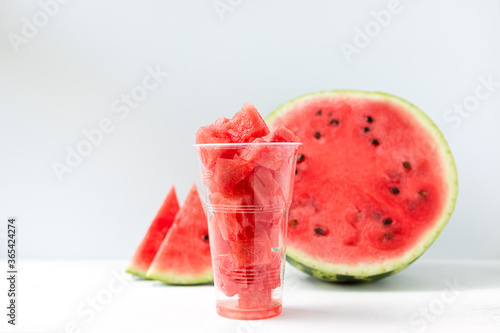 sliced pieces of ripe, juicy, sweet watermelon inside a long, plastic Cup on a light background front view. The concept of light, summer food.