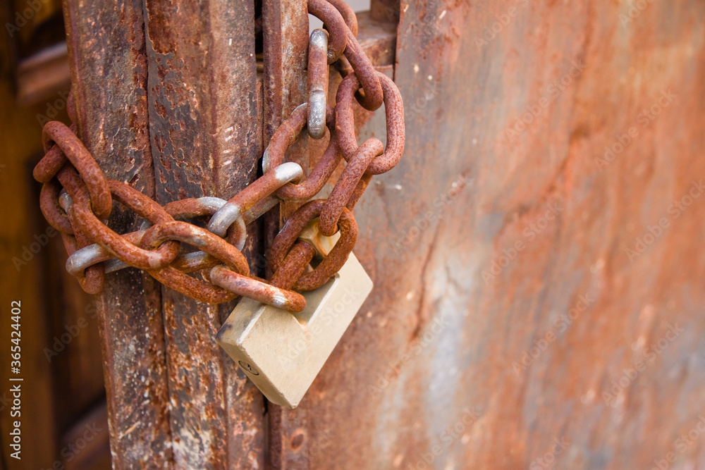 Rusty metal gate of a factory closed with padlock - concept image