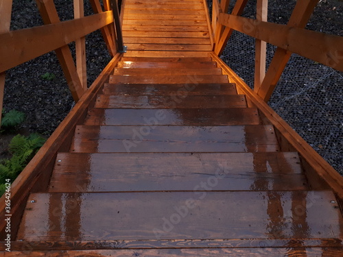 wet wooden stairs, wooden bridge in the rain in the evening is illuminated by beautiful light from lanterns, glare from a lantern on a wet tree